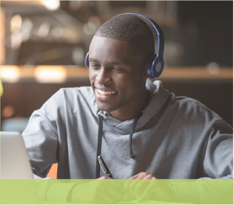Young man wearing headphones taking notes at a computer, smiling