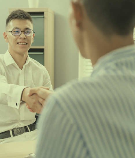 Two young men meet in a company office for an interview. They shake hands as they greet each other